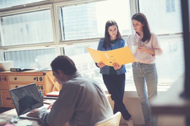 Two women discussing working plan in office. Man working on lapt